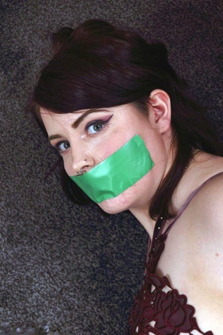 Clothed girl is silenced with a strip of tape over her mouth while tied up