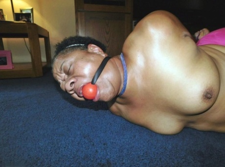 Overweight black woman Trixie struggles against a ball gag while hogtied