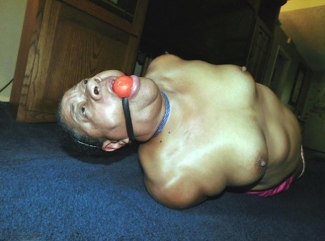 Overweight black woman Trixie struggles against a ball gag while hogtied