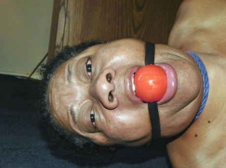 Overweight black woman Trixie struggles against a ball gag while hogtied