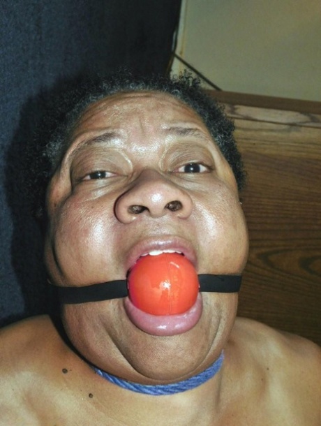 Overweight black woman Trixie struggles against a ball gag while hogtied