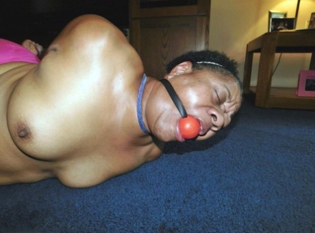 Overweight black woman Trixie struggles against a ball gag while hogtied