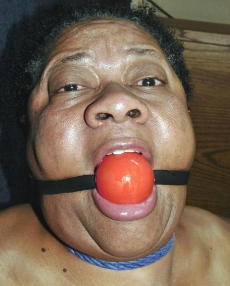 Overweight black woman Trixie struggles against a ball gag while hogtied